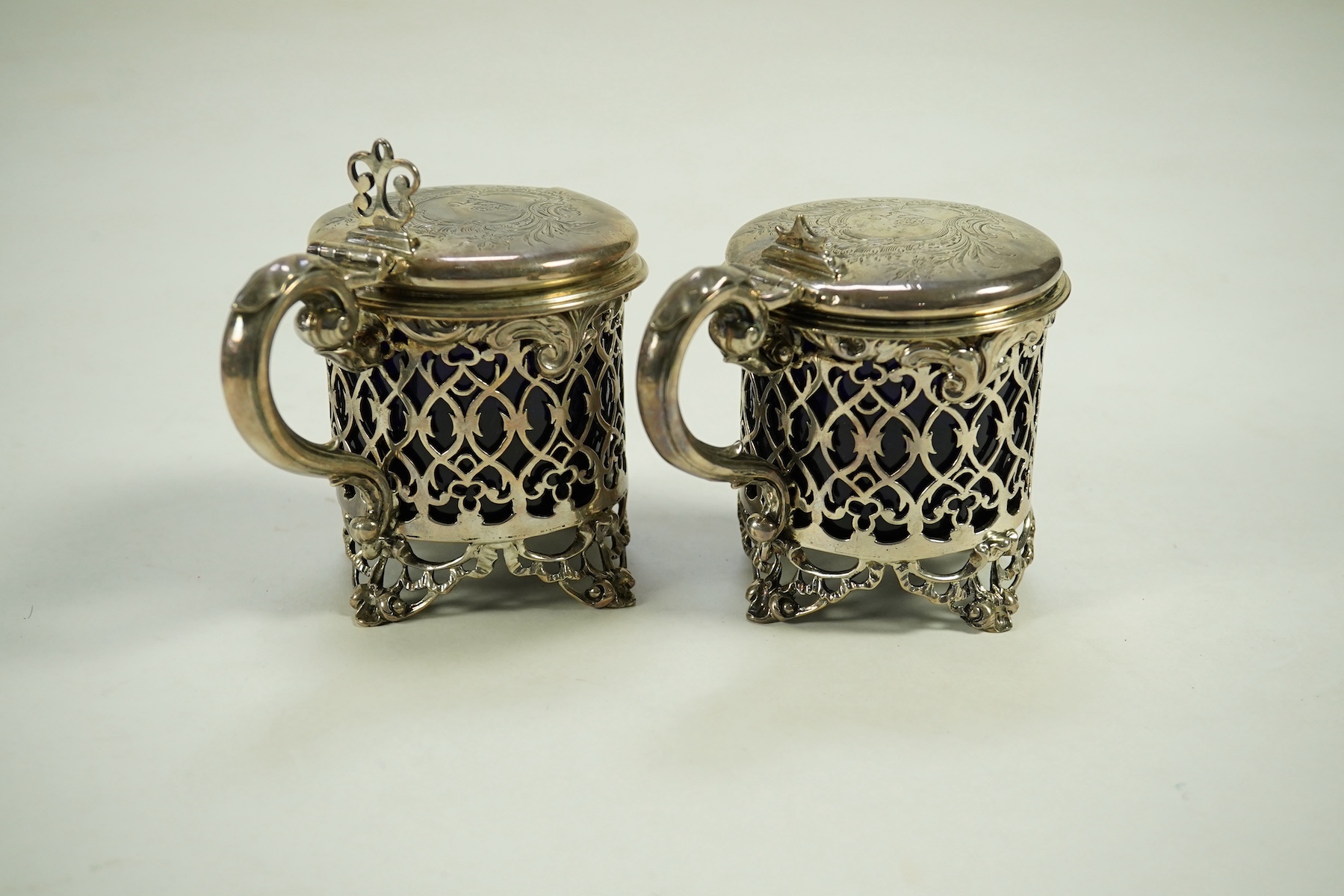 A near pair of ornate Victorian pierced silver drum shaped mustard pots and covers, one by Charles Thomas Fox & George Fox, the other by George Fox